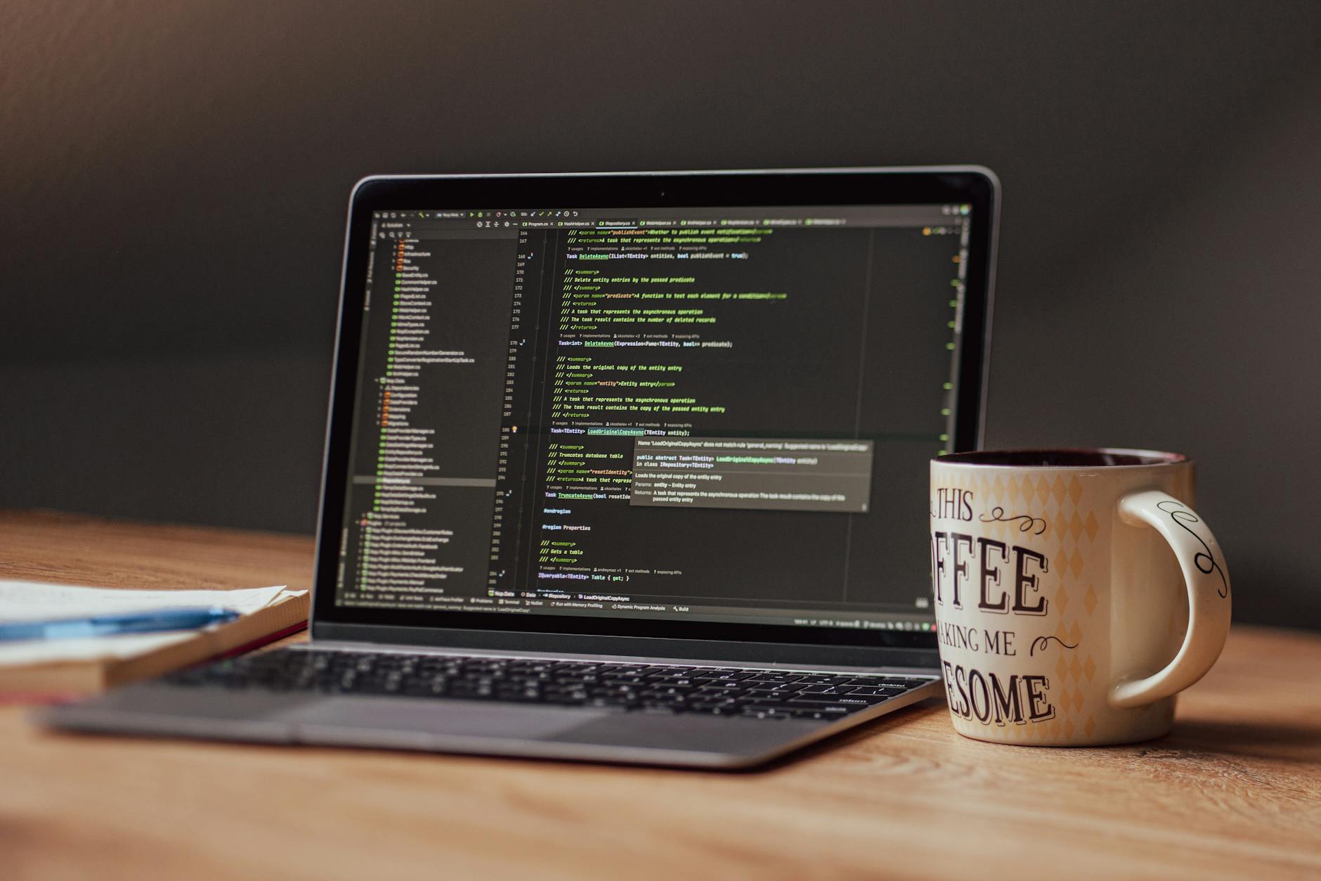Laptop on a desk with a code editor on screen and a coffee mug beside it